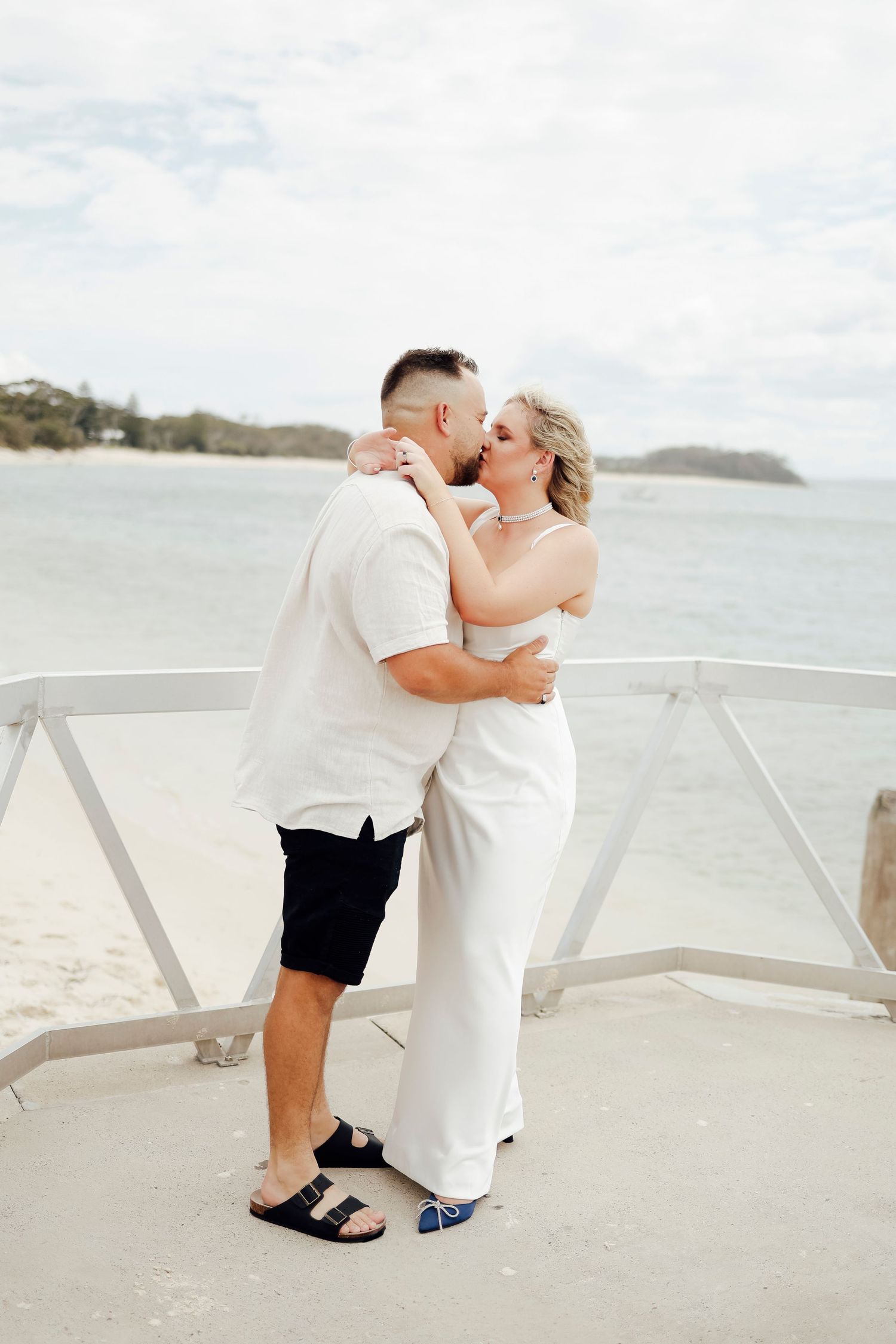 Couple sharing a romantic kiss on a beachside deck at Shoal Bay engagement shoot.