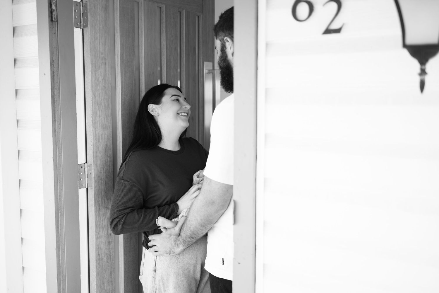Black and white photo of a couple embracing at a front door numbered 62.