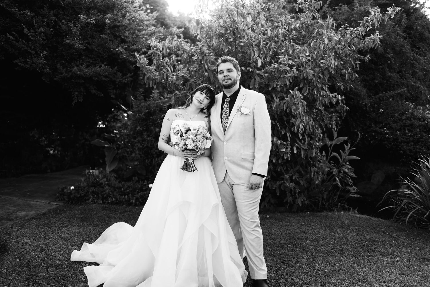 Bride and groom posing together in a lush garden setting on their wedding day in black and white.