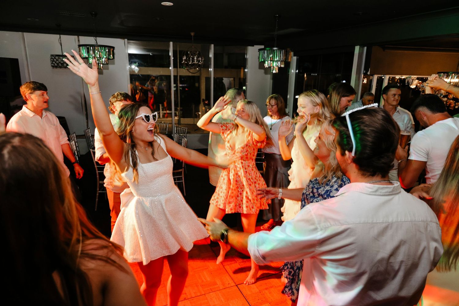 Energetic wedding guests dancing on a lit dance floor with orange lighting at a lively reception.