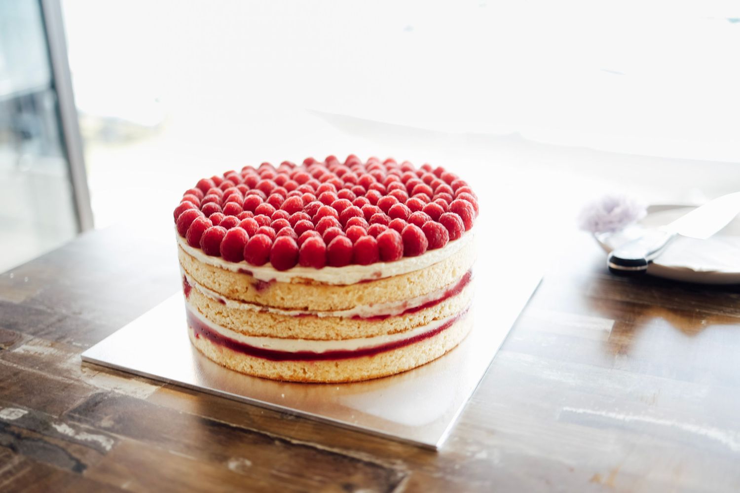 Elegant raspberry layer cake topped with fresh raspberries on a wooden table.