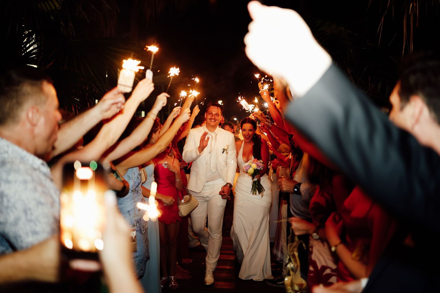 Bride and groom walking through sparkler tunnel during festive wedding send-off.
