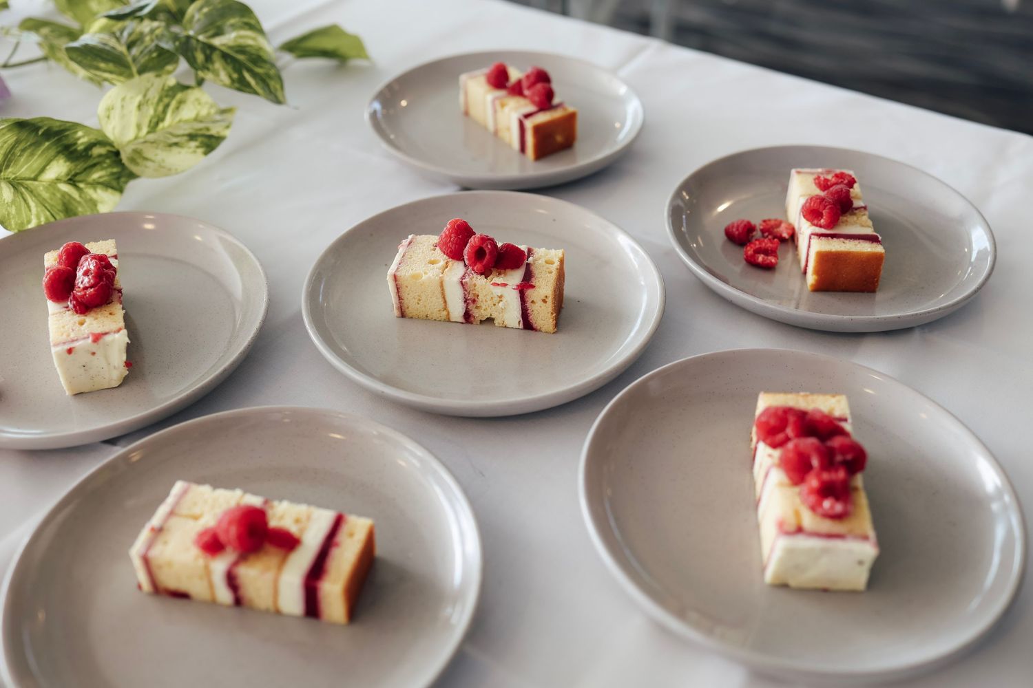 Six plated slices of raspberry cheesecake served on grey plates on a white surface.