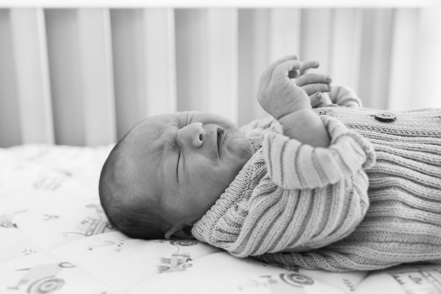 Black and white photo of a newborn baby lying in a crib wearing a knit sweater.