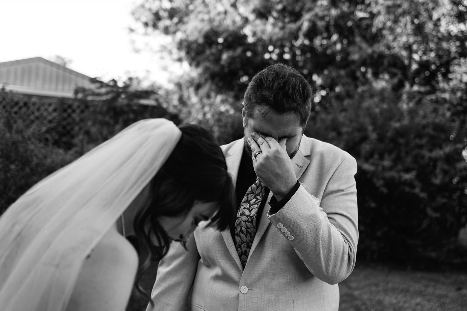 Emotional black and white photo of bride and groom sharing a tender moment outdoors.