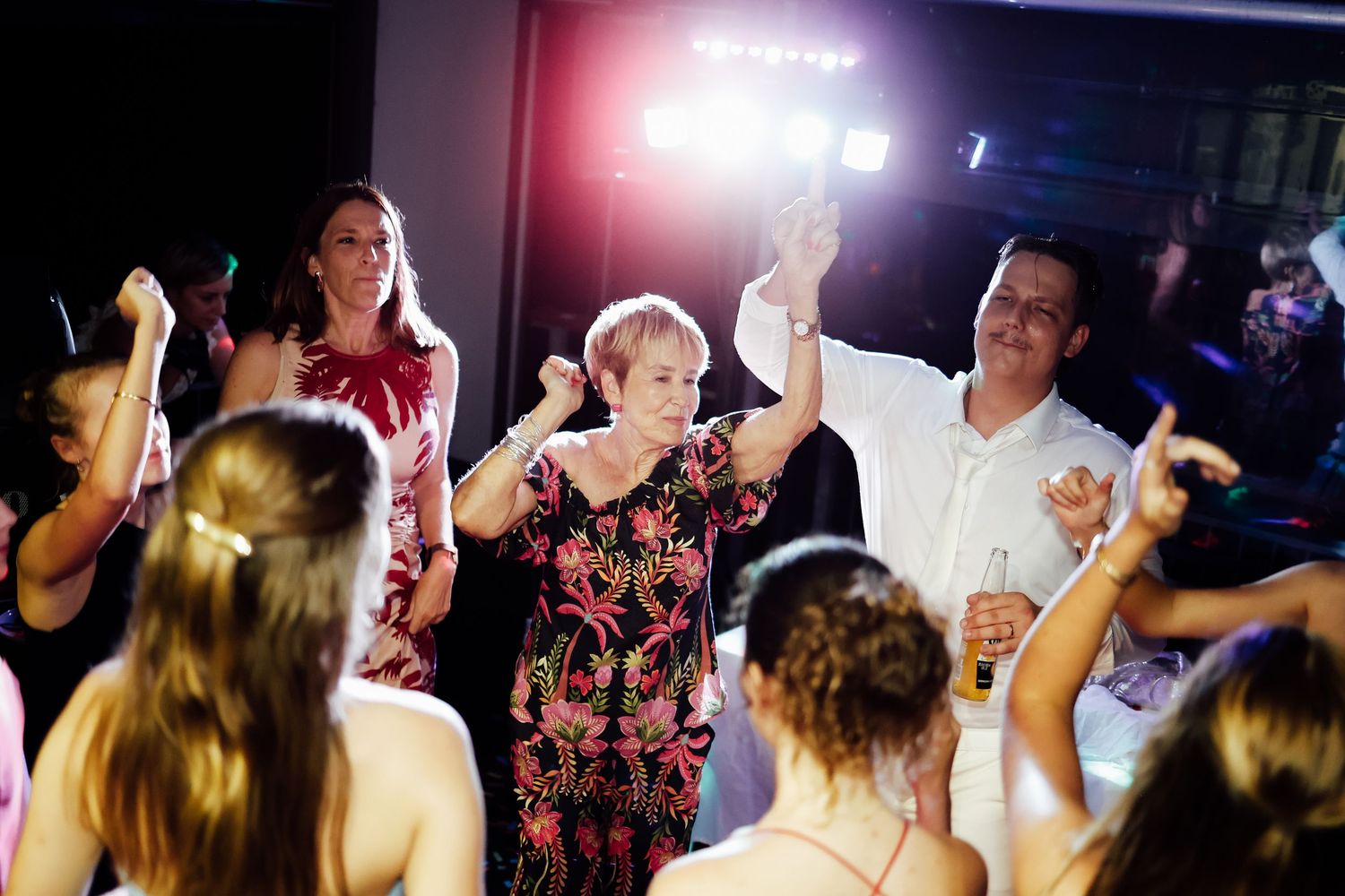 Guests dancing joyfully at a wedding reception under colorful stage lights.