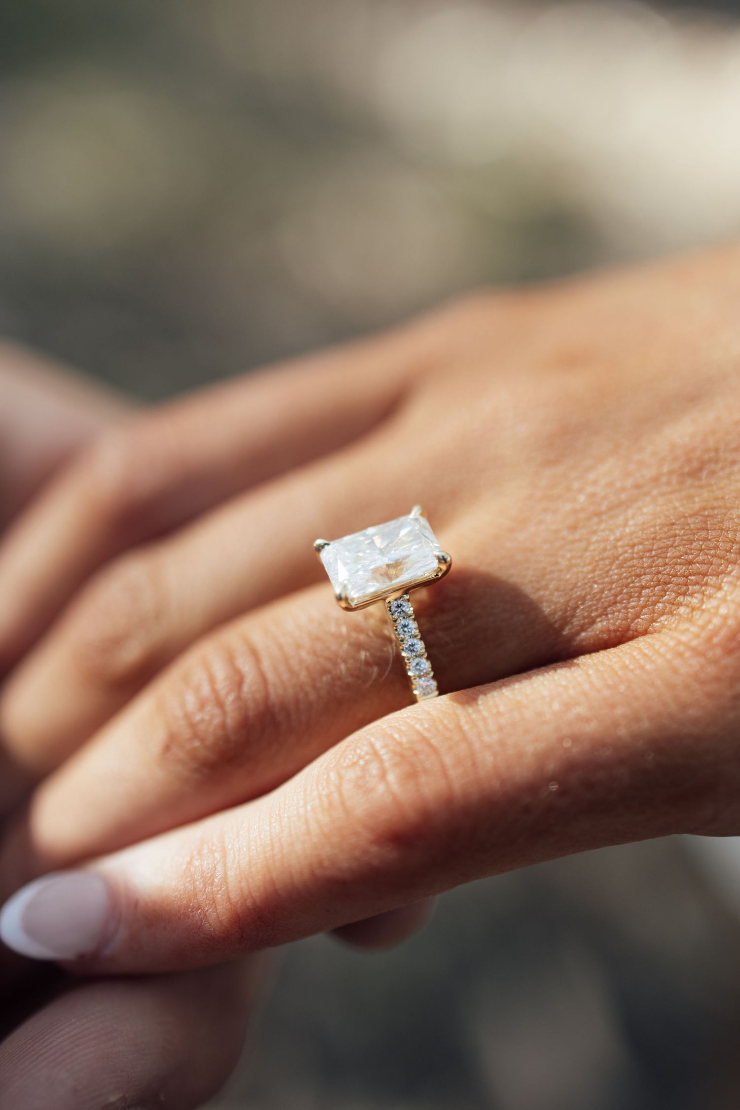 Close-up of a radiant cut diamond engagement ring with pavé band on a gold setting.