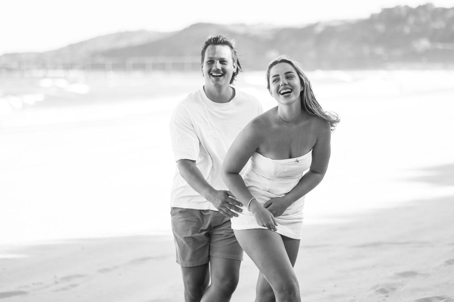 Joyful couple laughing together while walking on a beach in a black and white photo.