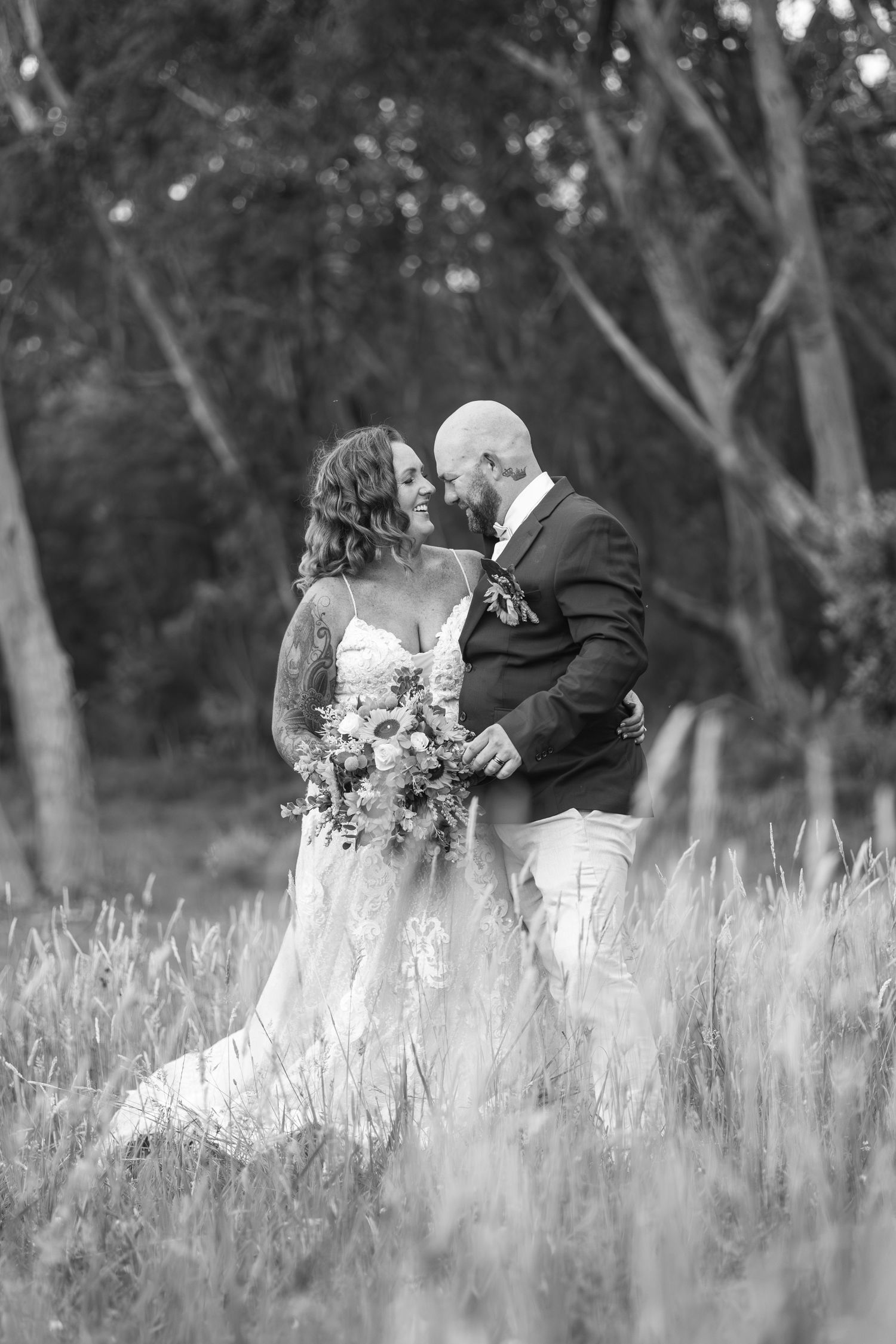 Romantic black and white photo of bride and groom embracing in tall grass field.