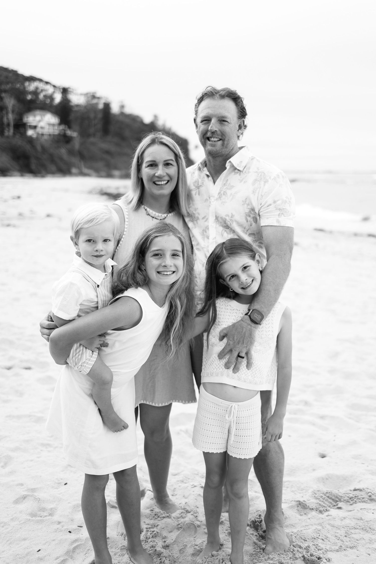 Happy family of five posing together on a sandy beach in a black and white portrait.