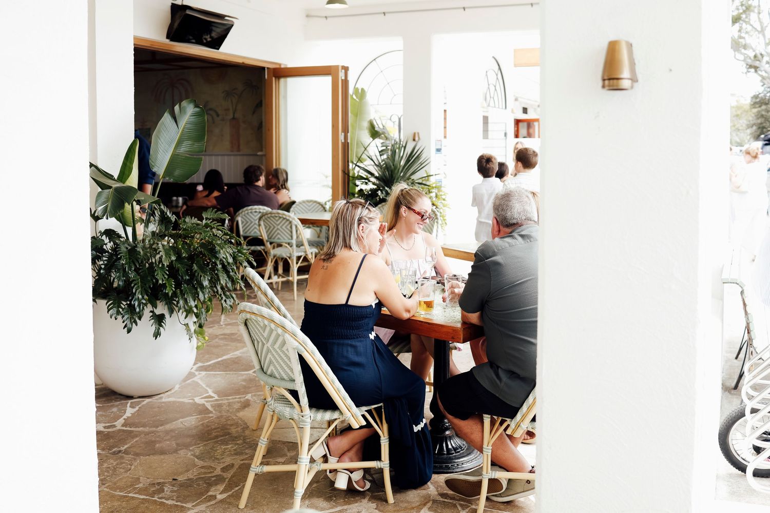 Woman in navy dress dining at a bright coastal restaurant with lush plants.