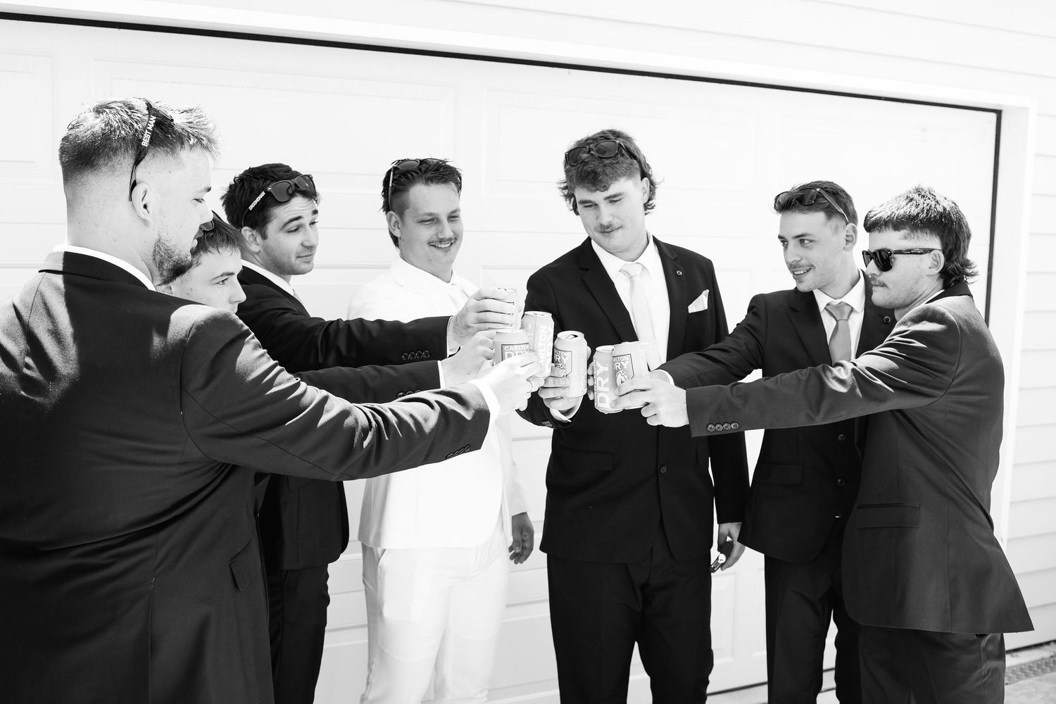 Groomsmen in black suits toasting with drinks in a black and white wedding photo.