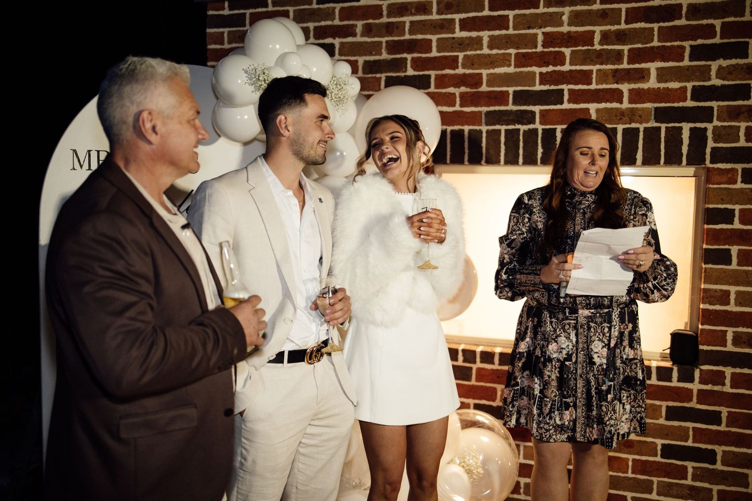 Engaged couple in white outfits laughing with guests at their engagement celebration.