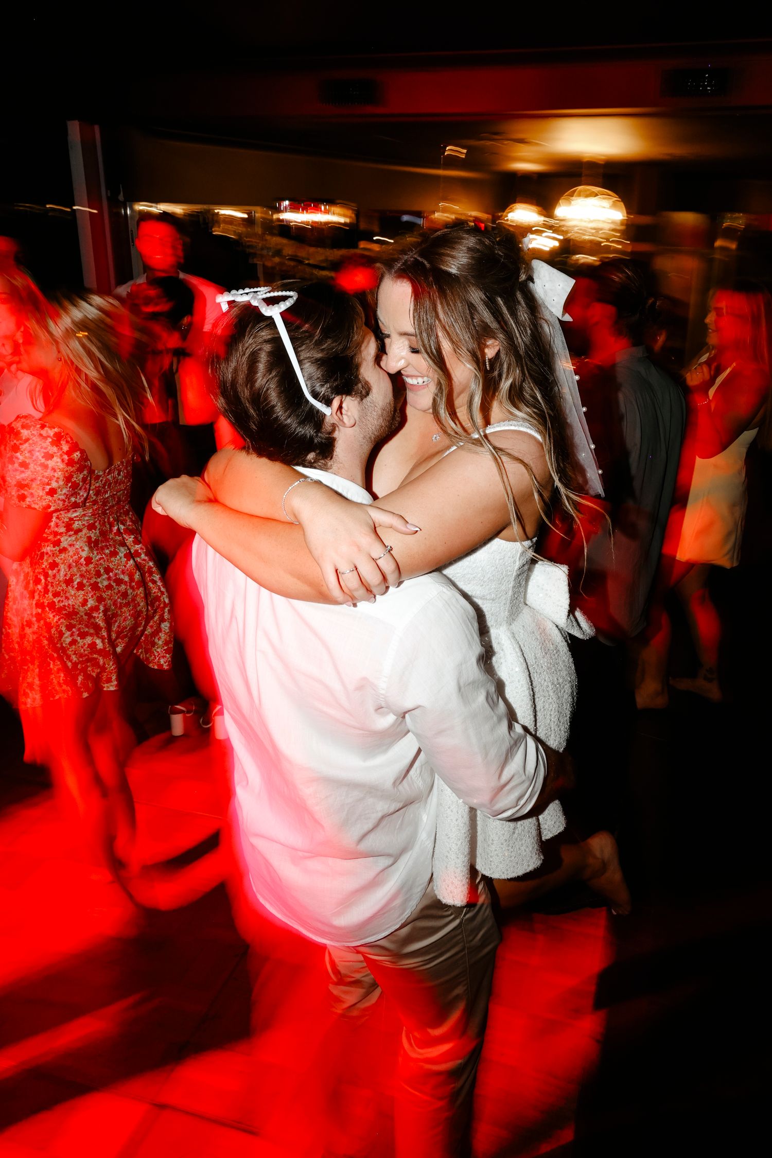 Bride and groom sharing an intimate embrace while dancing under red romantic lighting at reception.