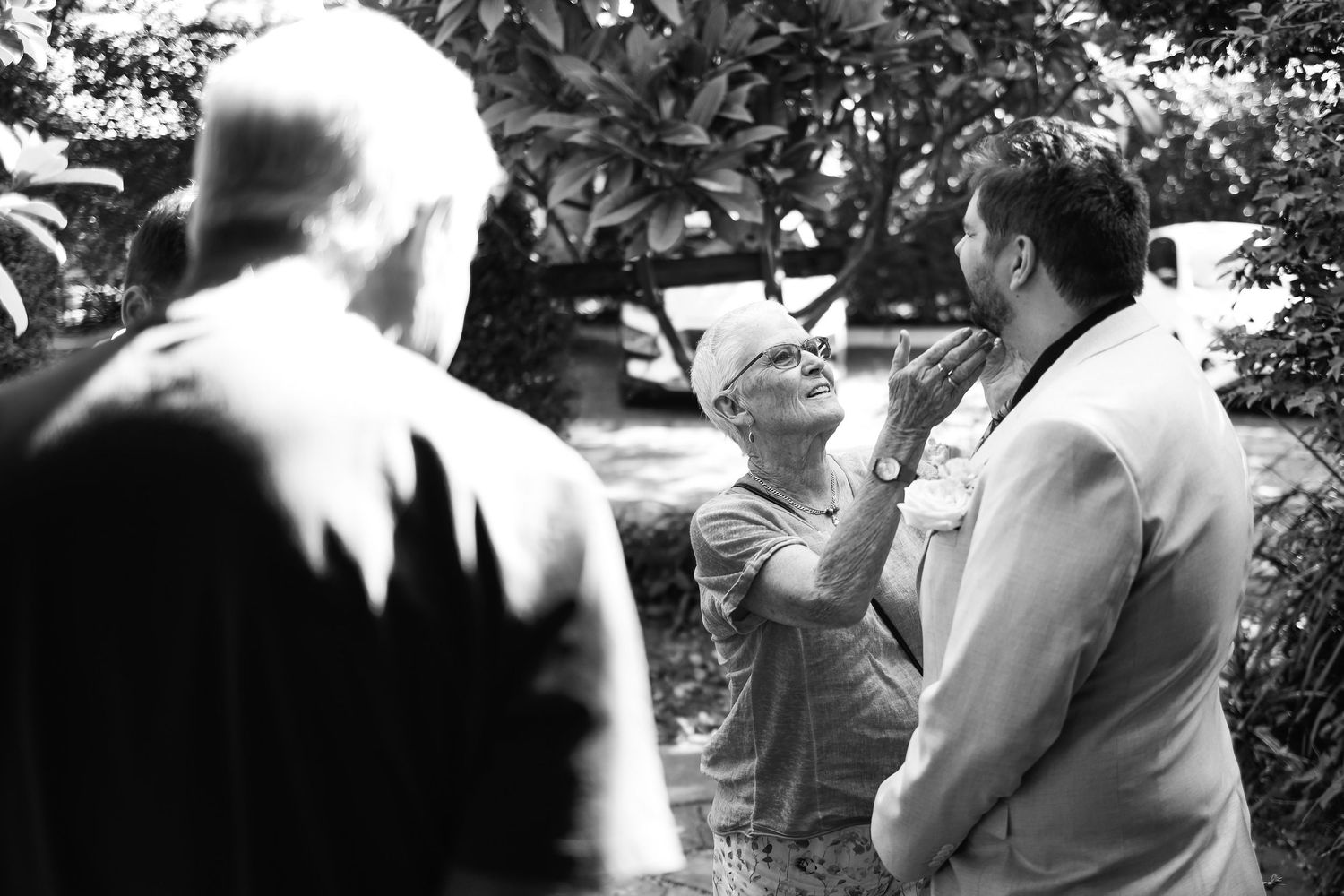 Black and white photo of three men conversing outdoors among lush trees and foliage.