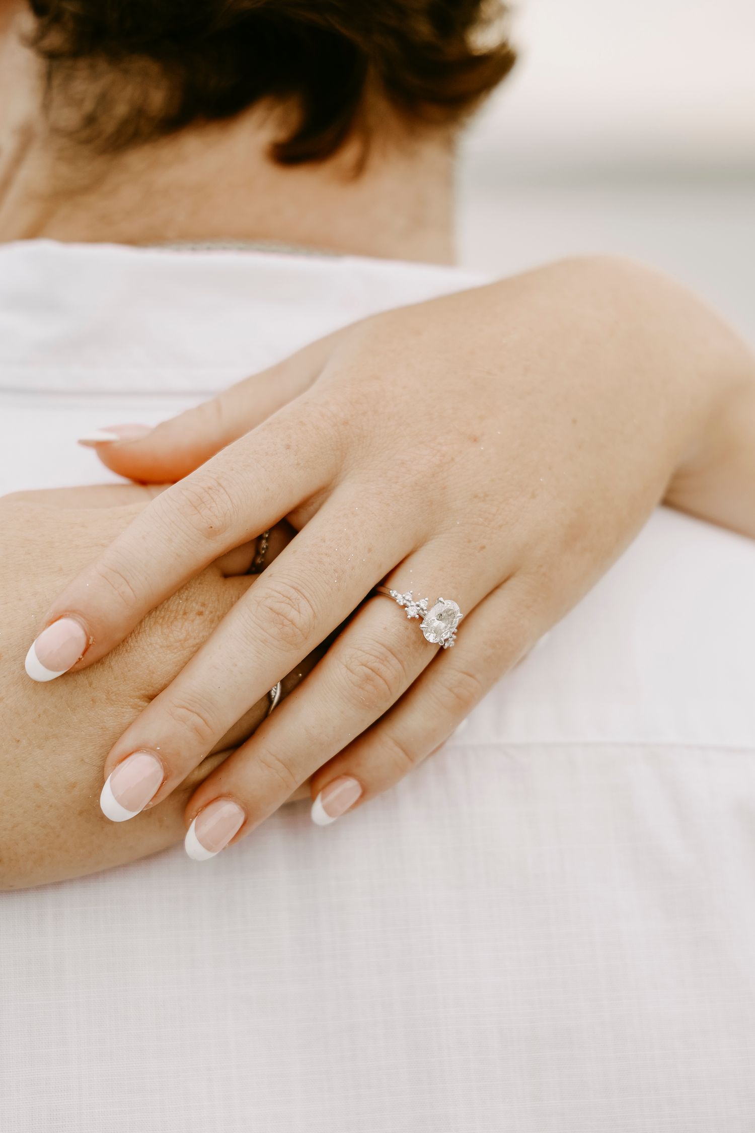 Close-up of a womans hand displaying a stunning oval diamond engagement ring on her partners back.