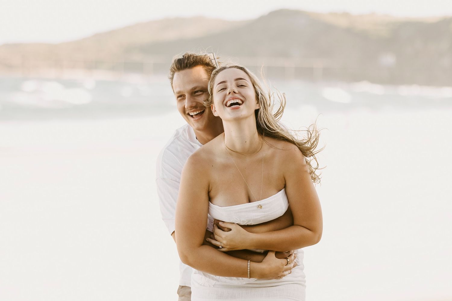 Joyful couple embracing and laughing on a scenic beach.