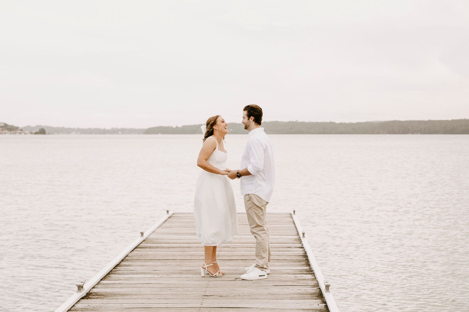 Bride and groom sharing a romantic moment on a wooden dock by the lake.