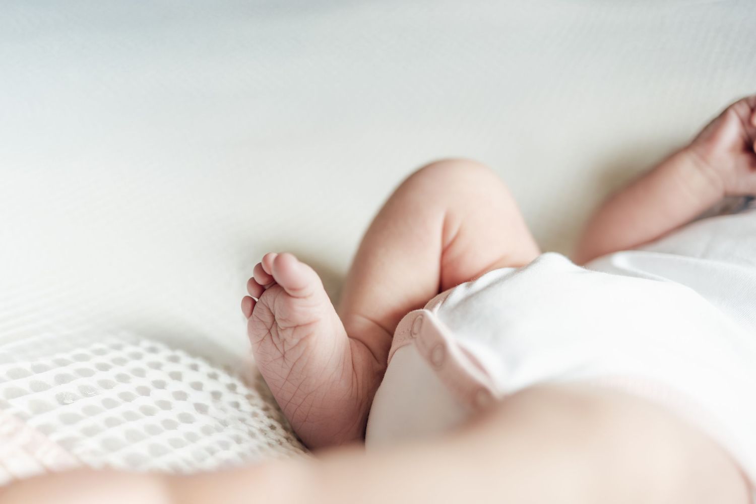 Close-up of adorable chubby baby feet and legs resting on a soft white textured blanket.