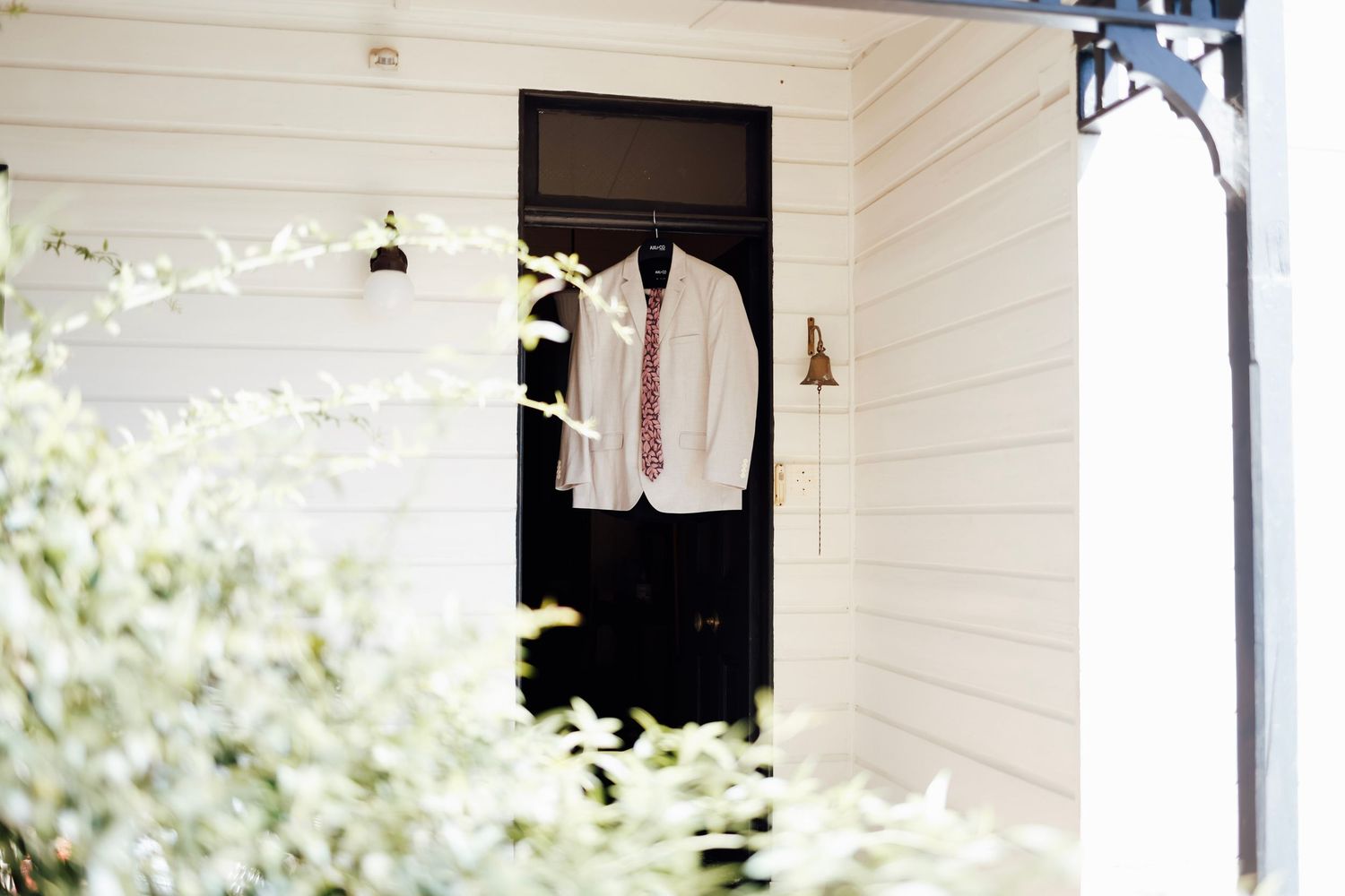 White suit jacket with red tie hanging on a black door of a white wooden house exterior.