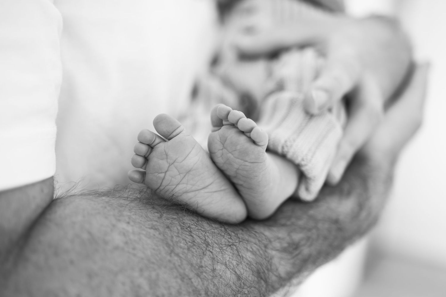 Black and white photo of a newborn baby's tiny feet cradled gently in an adult's hands.