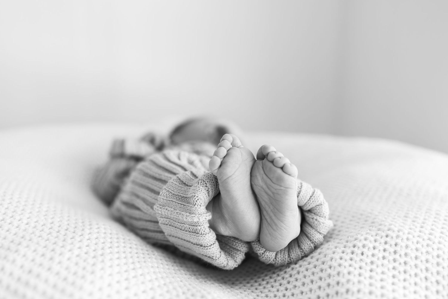 Black and white photo of a sleeping newborn baby wrapped in a knit sweater, tiny feet visible.
