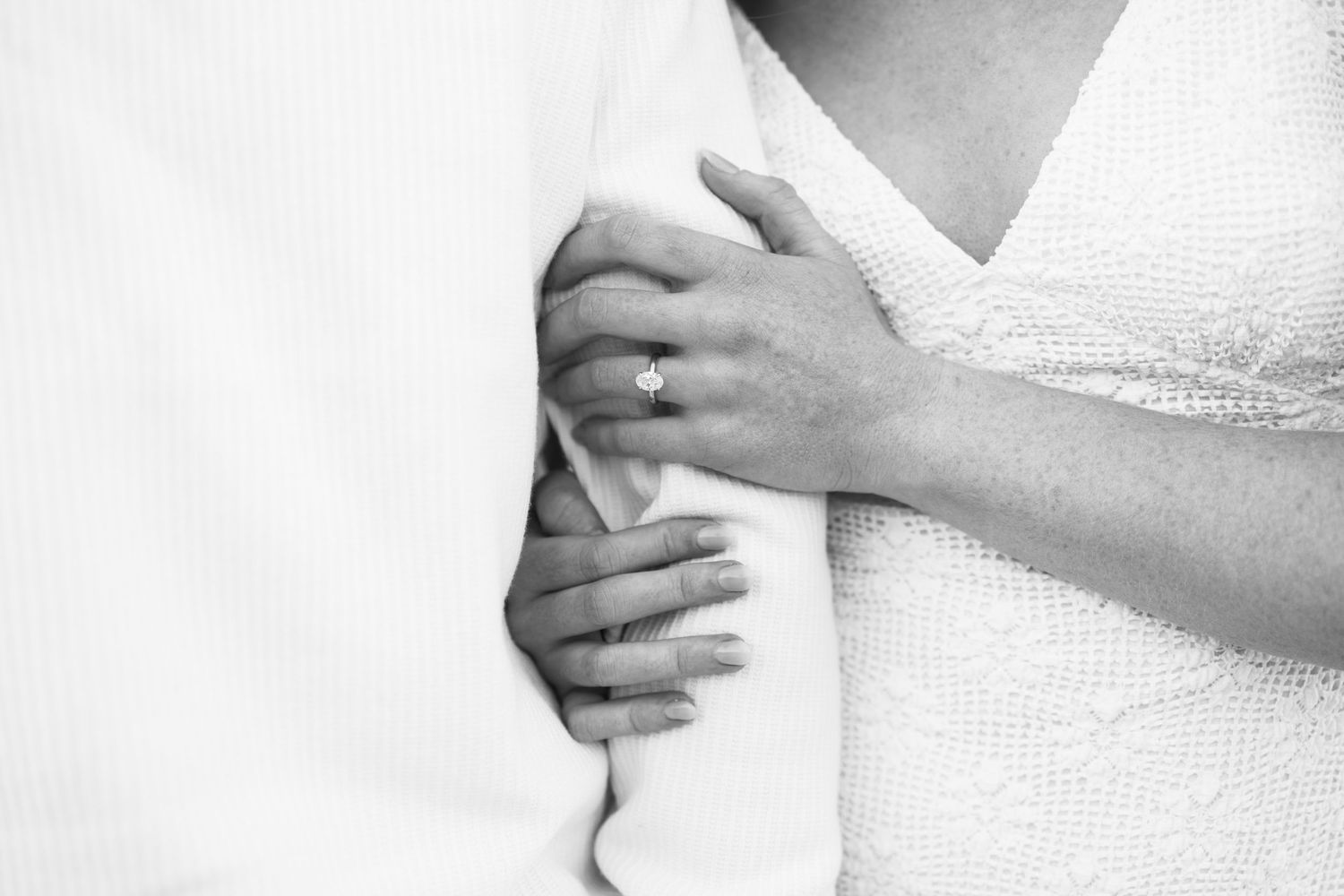 Black and white photo of a bride and groom embracing, showcasing an elegant diamond engagement ring on the bride's hand.