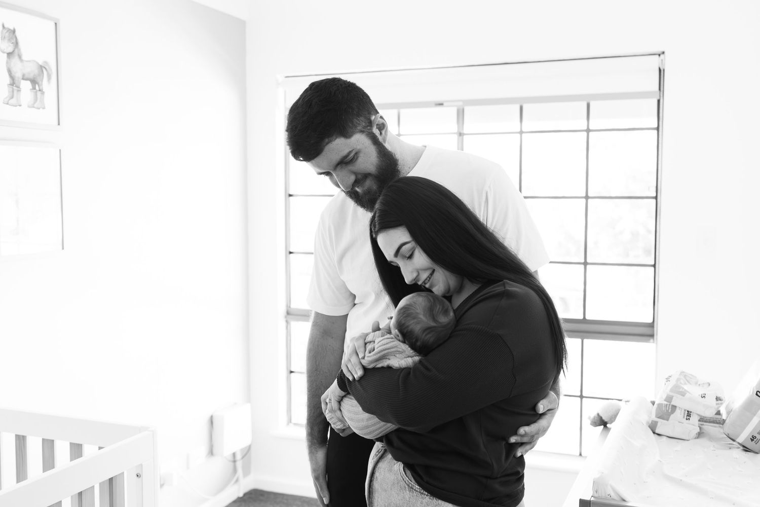 Black and white photo of parents tenderly holding their newborn baby in a nursery.