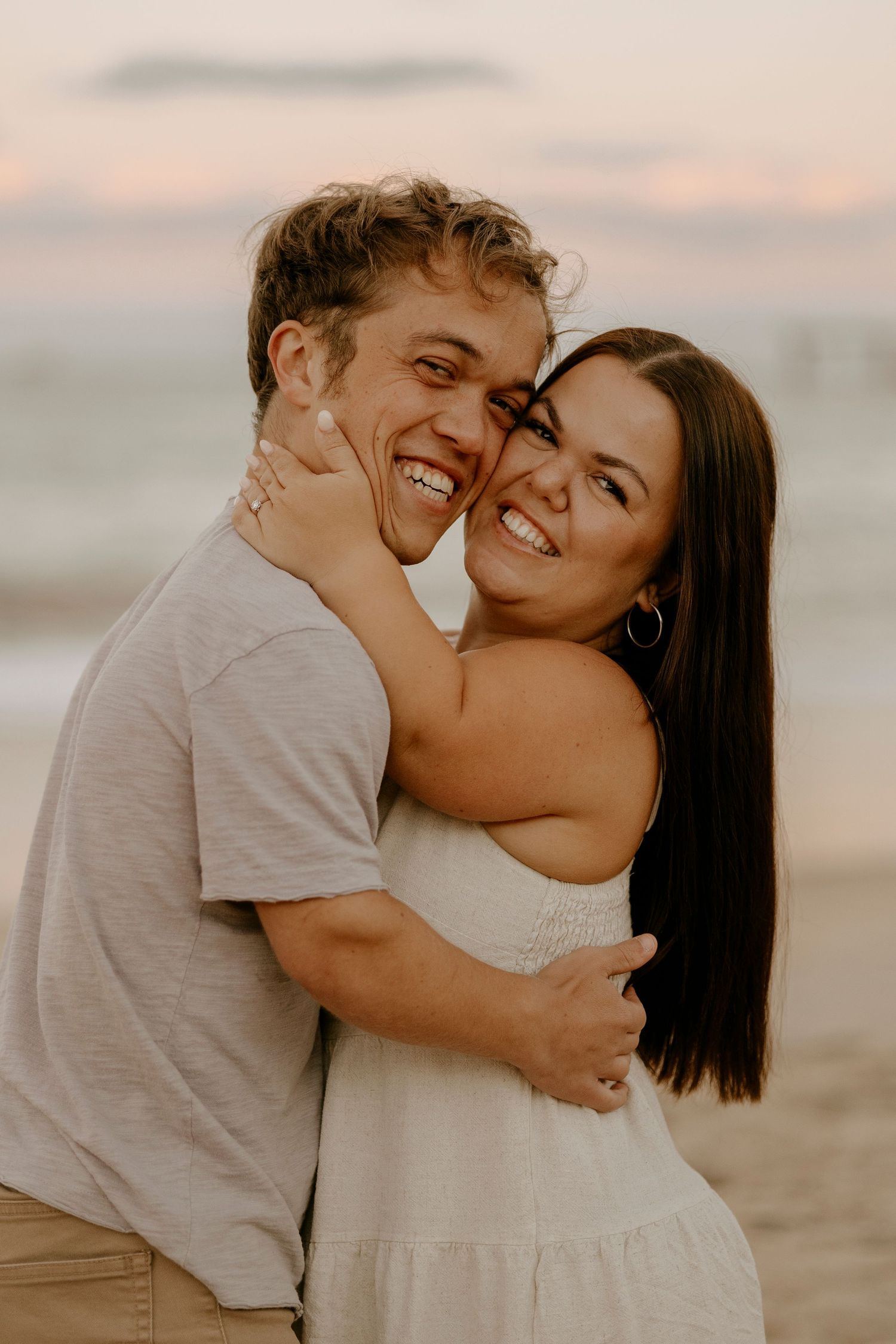 Joyful couple hugging and laughing together on a beach during a golden sunset.