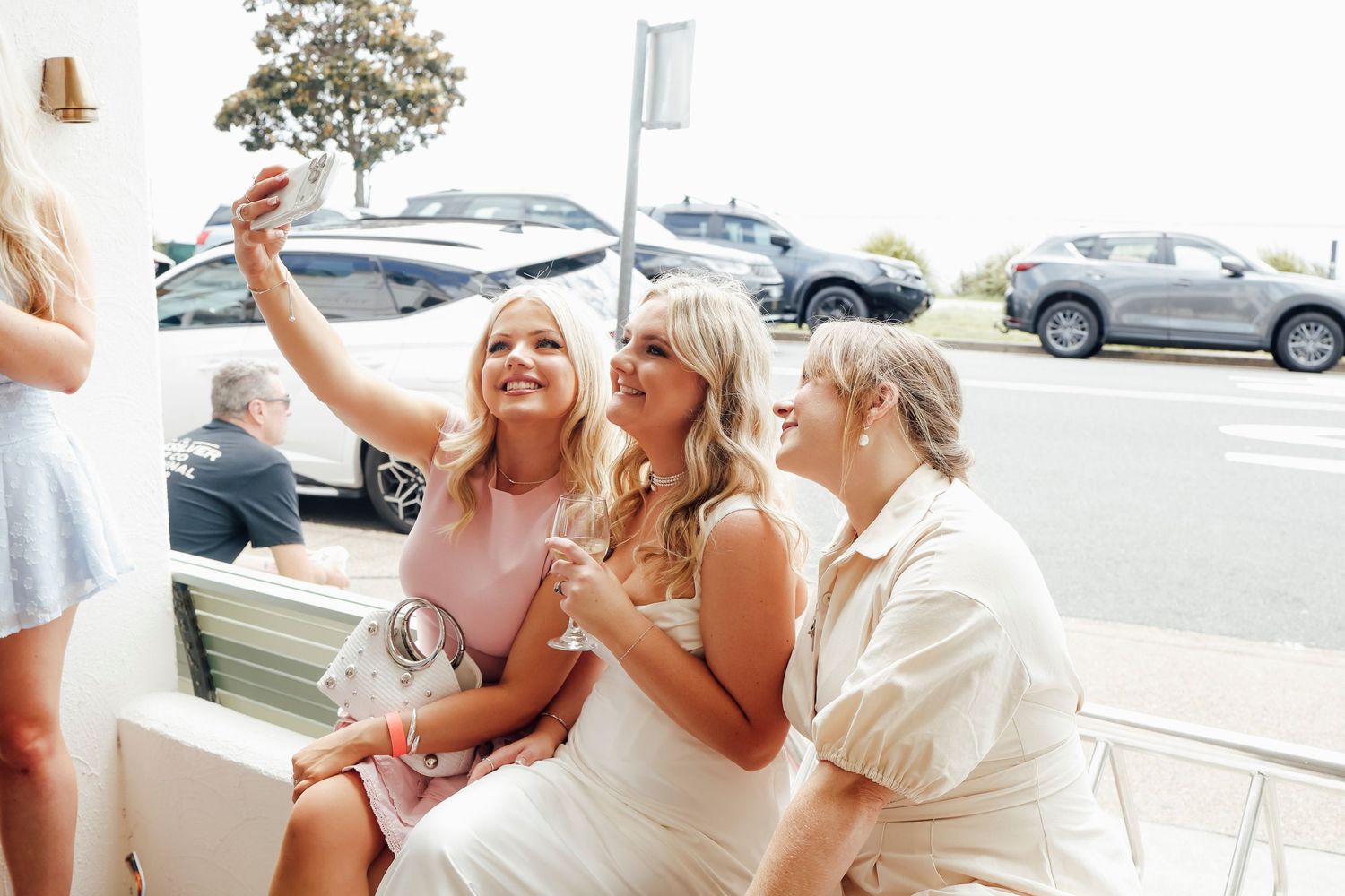 Three women taking a selfie together at a wedding venue outdoors.