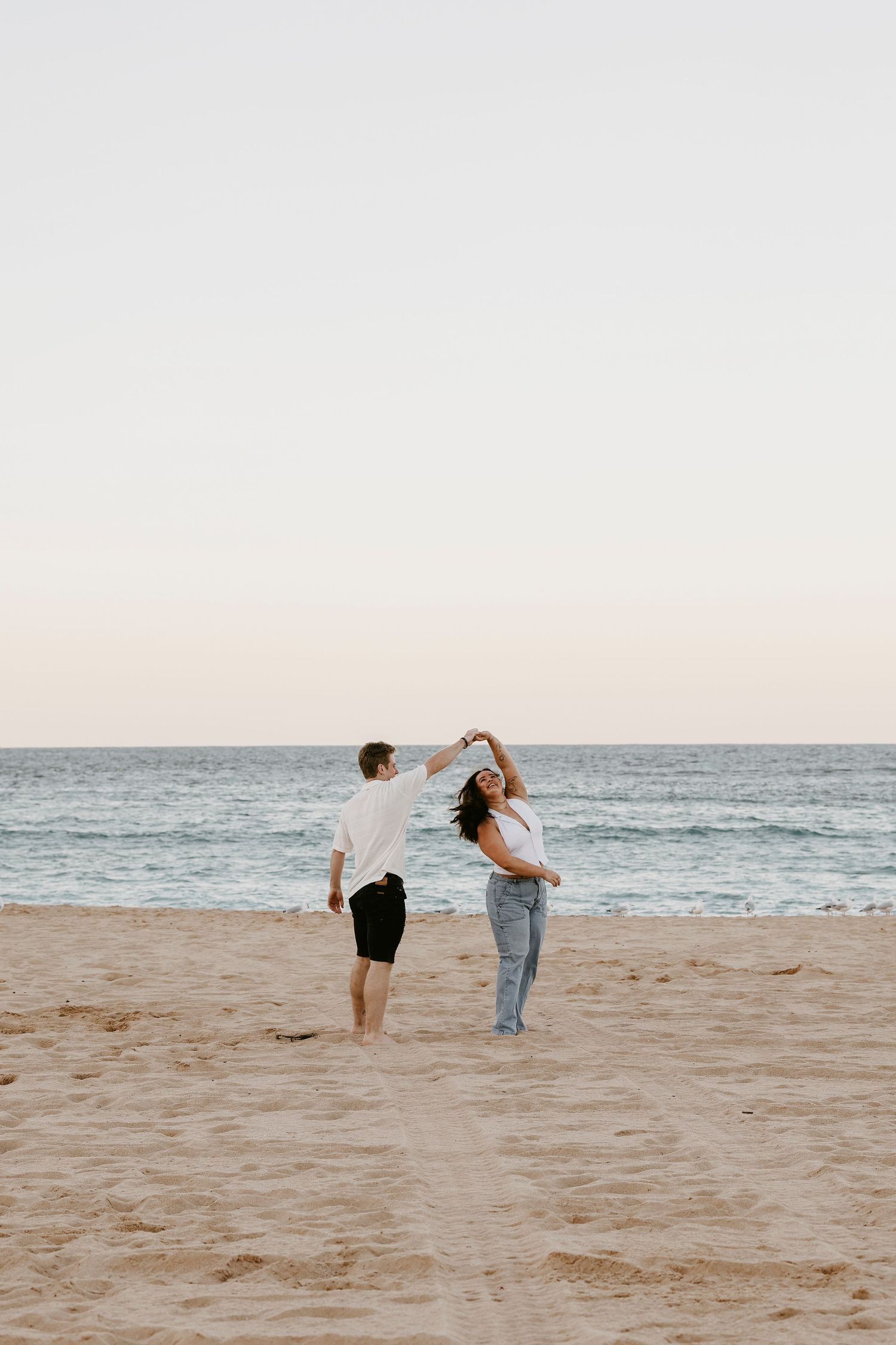 Couple dancing together on sandy beach at sunset with ocean waves in background.