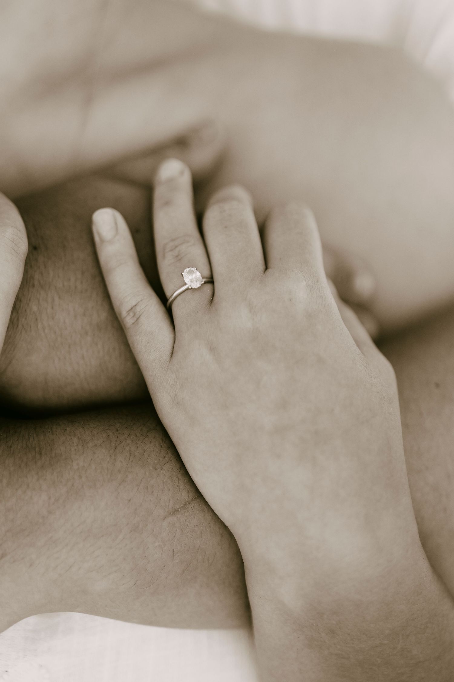 Close-up sepia-toned image of a hand wearing a delicate solitaire diamond engagement ring.