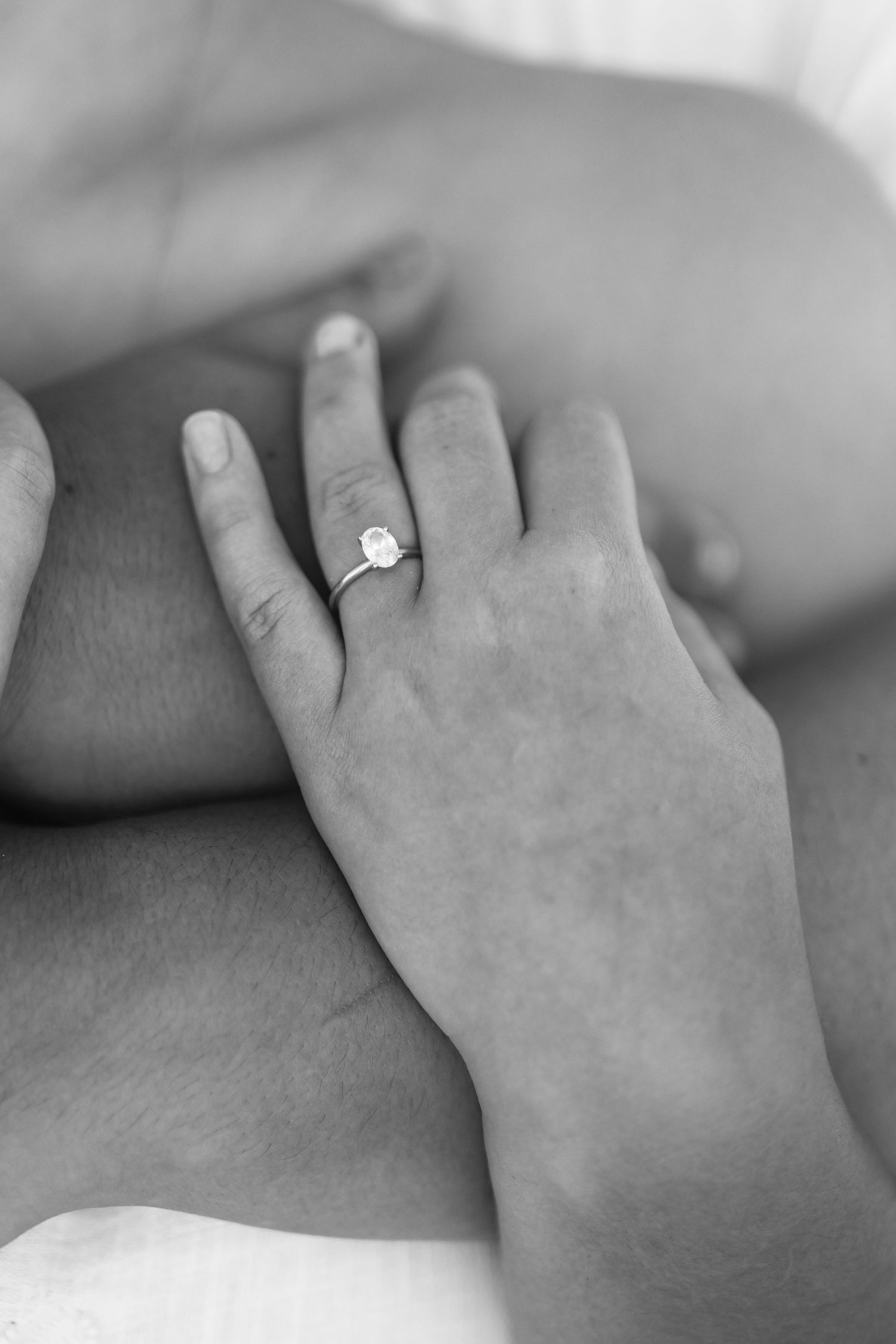 Black and white close-up of a womans hand wearing a diamond engagement ring.