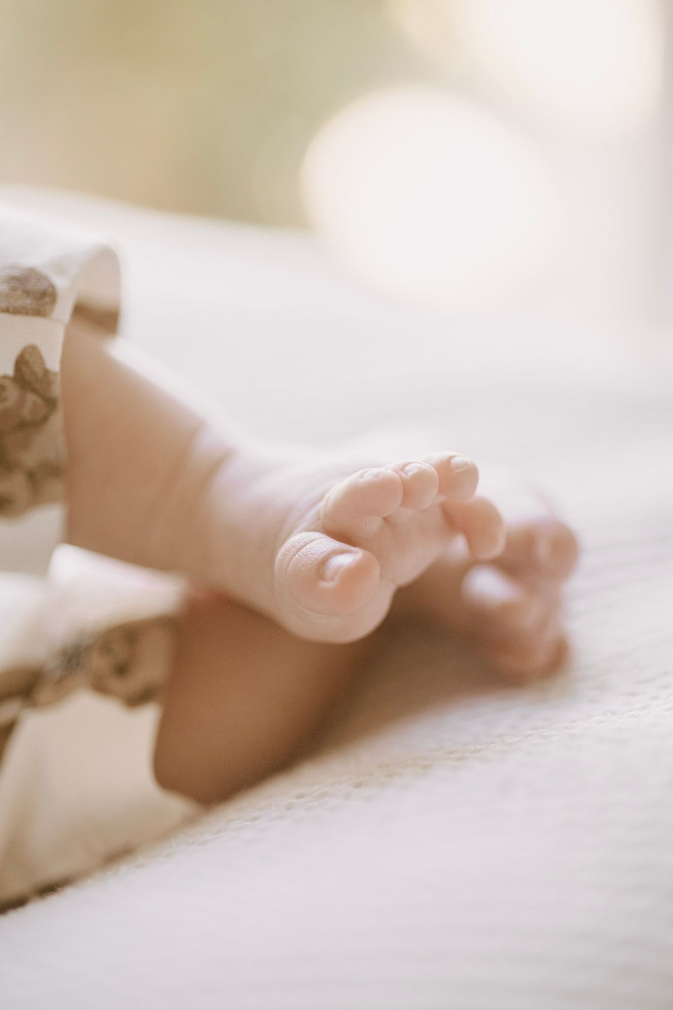 Soft focus close-up of newborn baby feet crossed on white blanket in warm light.