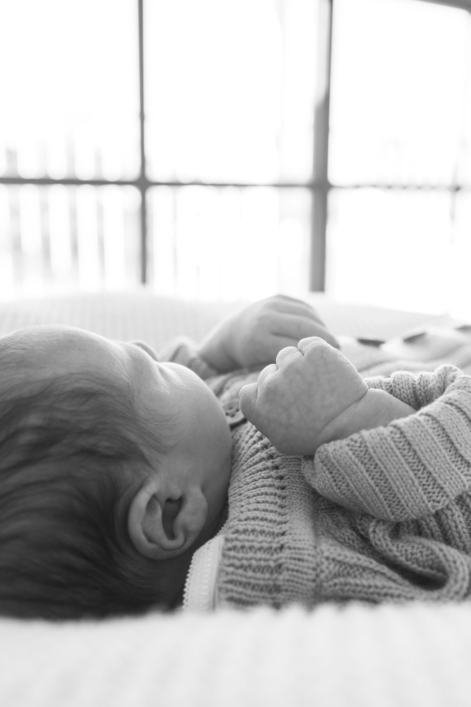 Black and white photo of a sleeping newborn baby in a knit sweater lying on a white blanket.