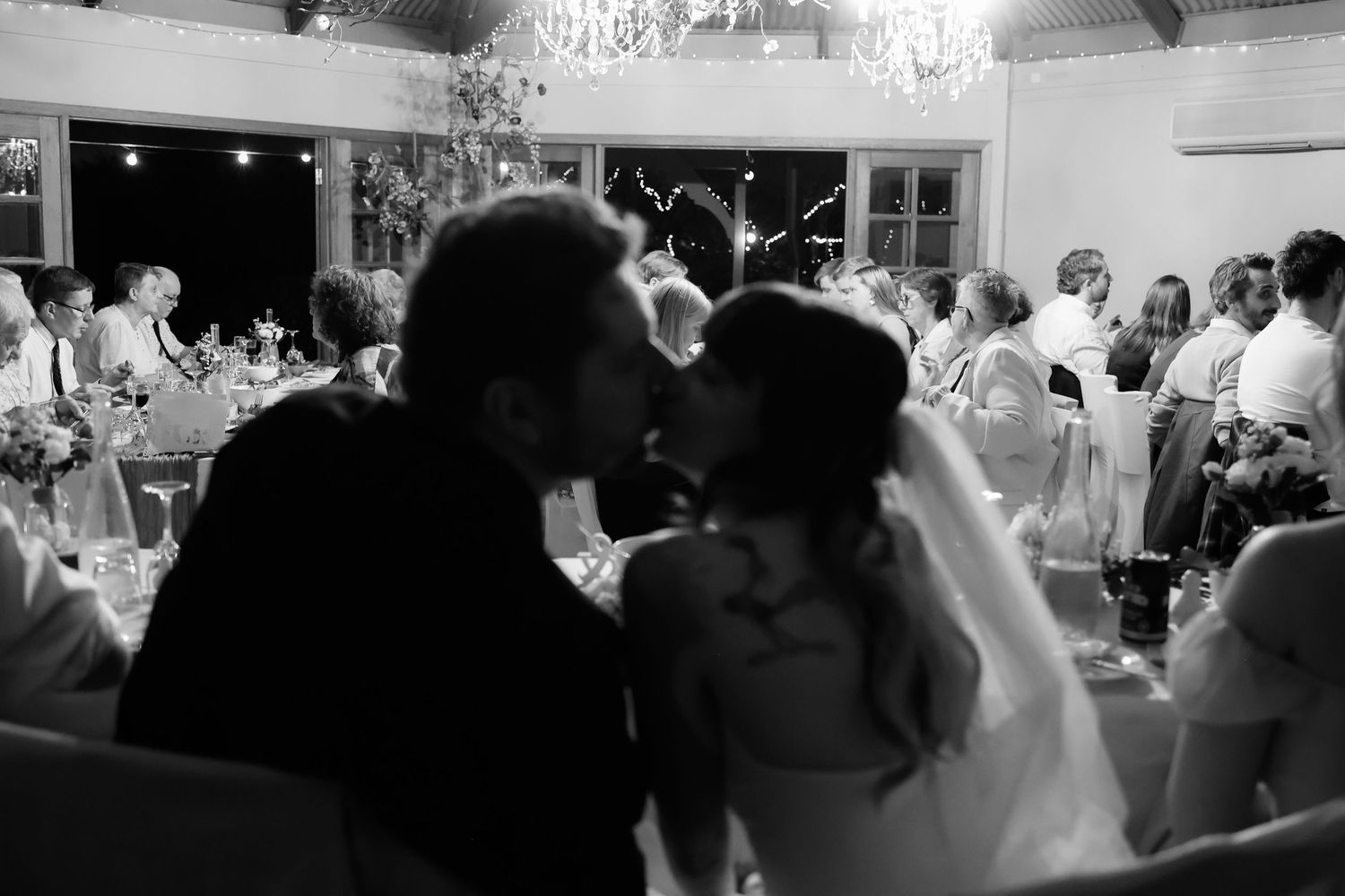 Romantic black and white silhouette of bride and groom sharing a kiss during wedding reception.