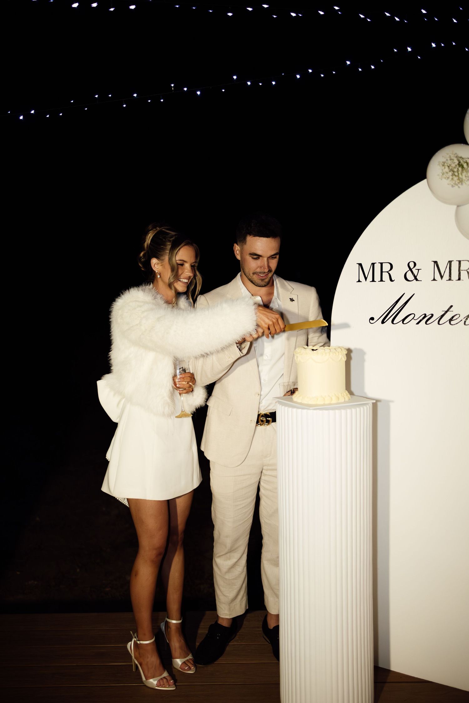 Couple in white cutting their engagement cake beside Mr & Mrs Monteleone arch sign.