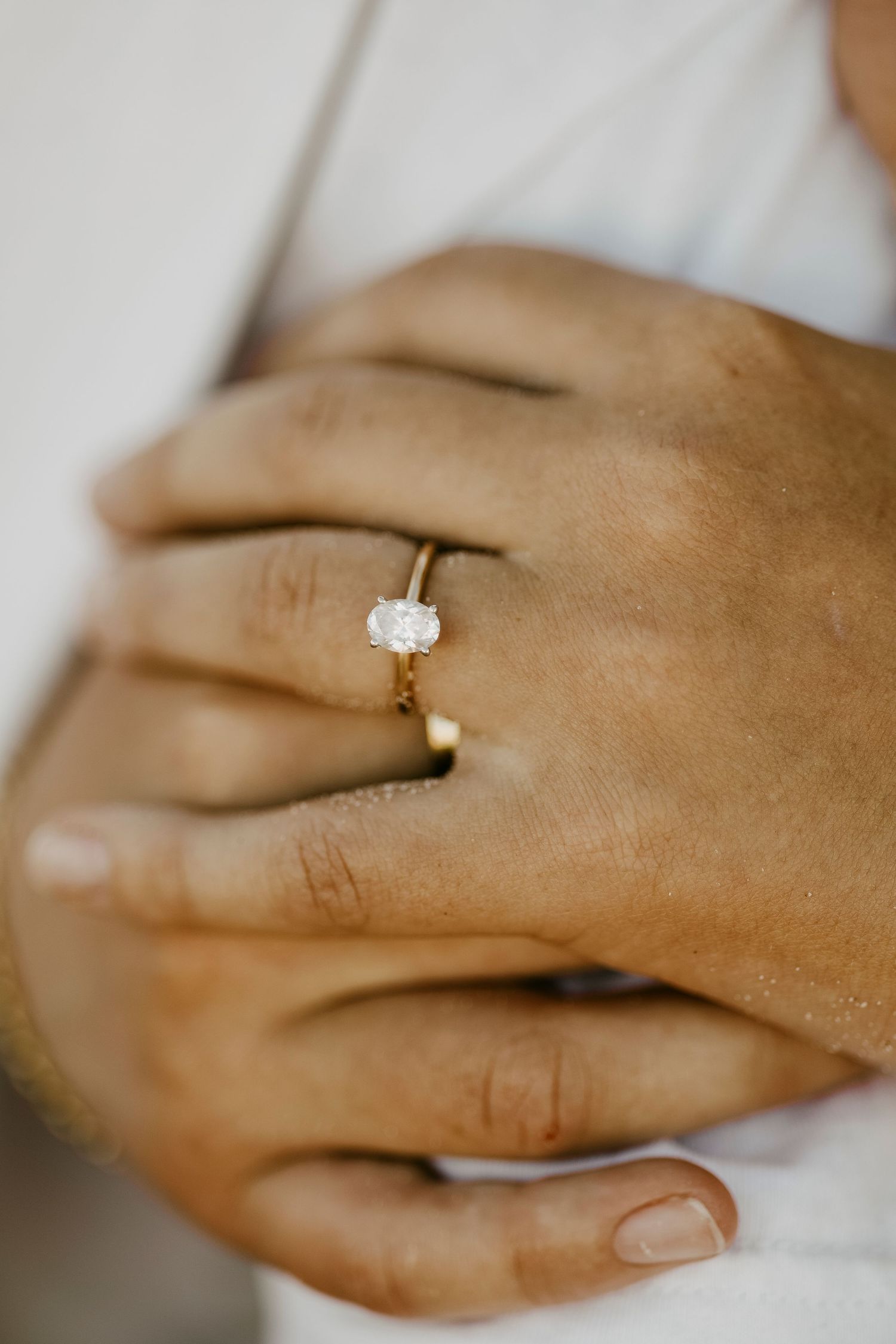Close-up of a gold oval diamond solitaire engagement ring on a womans hand.