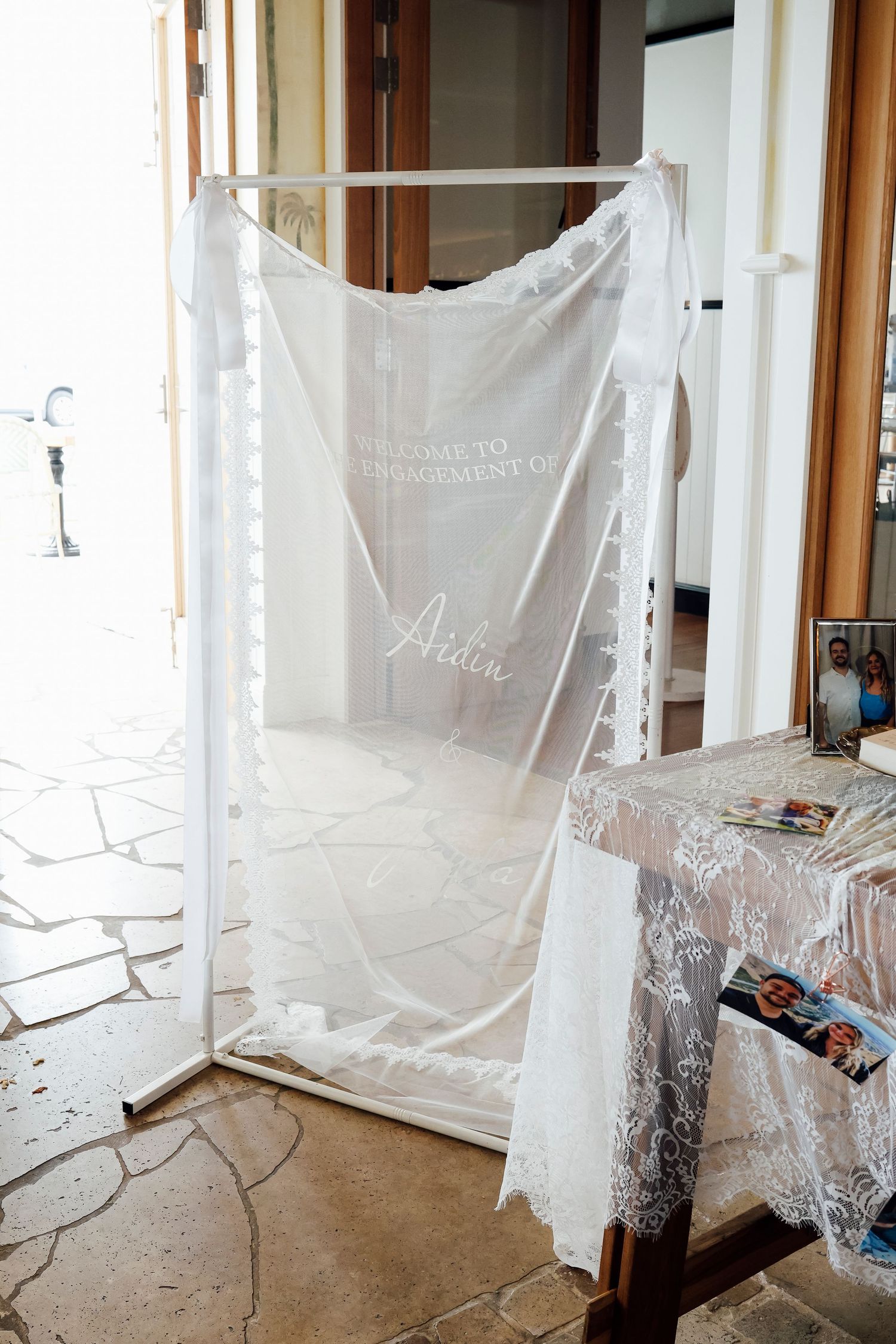 White sheer fabric sign welcoming guests to an engagement party displayed on a rack.
