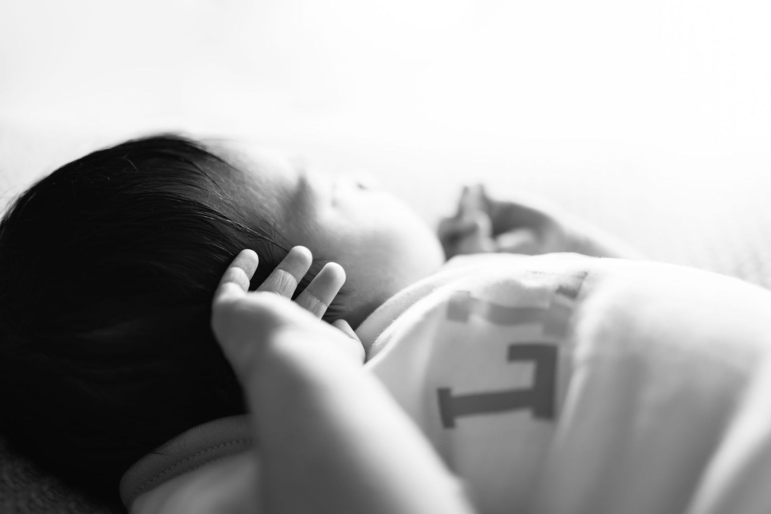Black and white photo of a sleeping newborn baby resting peacefully with hand near face.