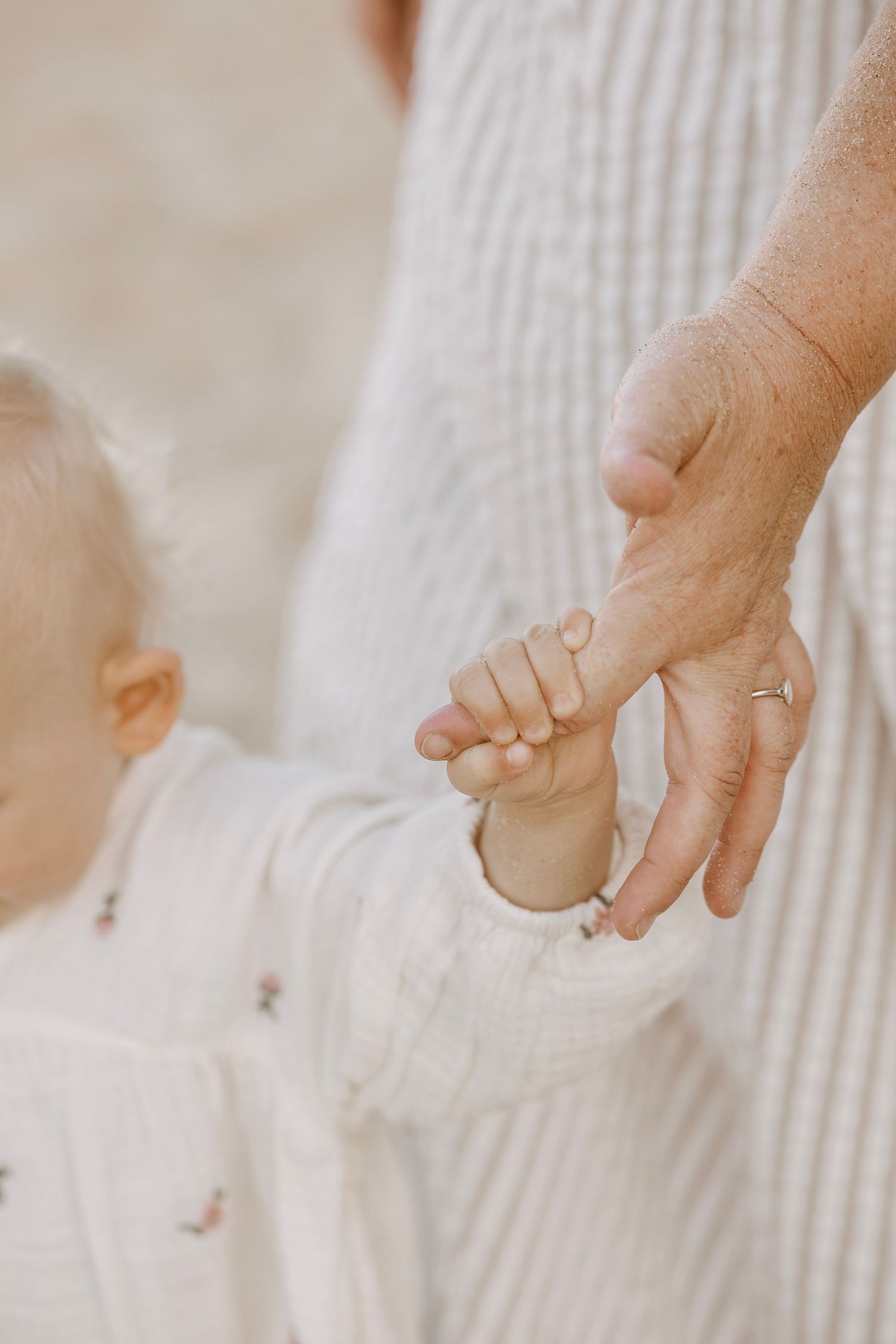 Close-up of baby holding mothers finger outdoors in soft natural light.
