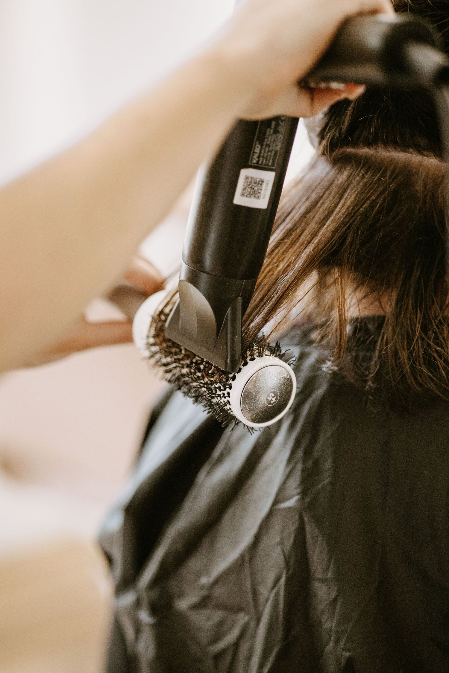 Hairstylist blow-drying and brushing a clients dark hair in a salon.