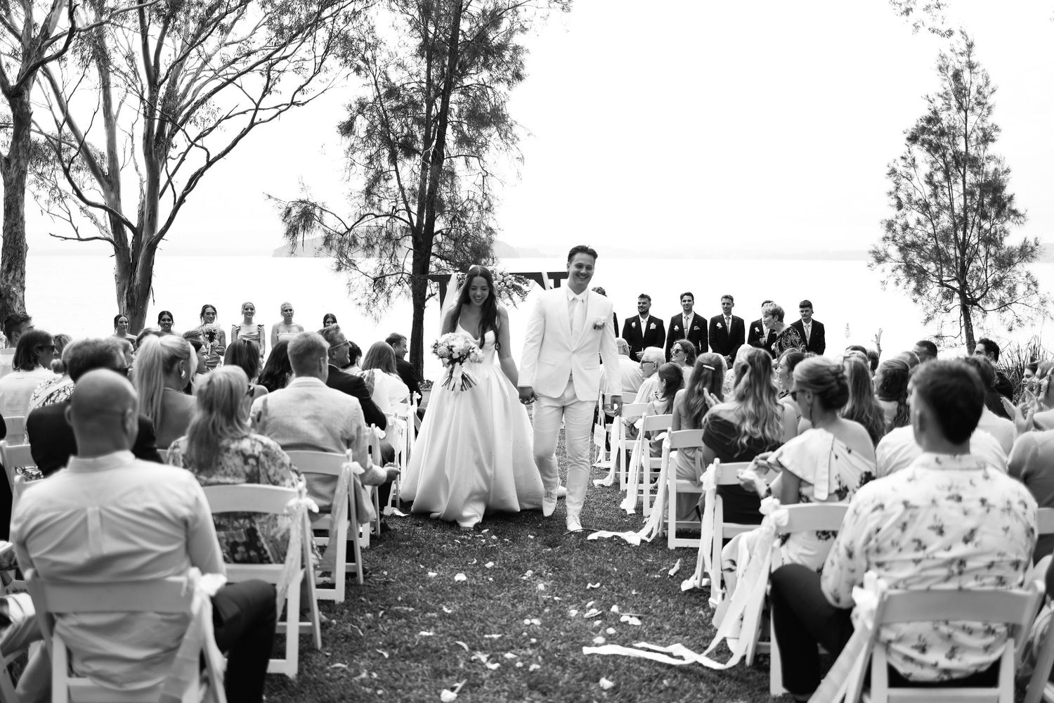 Bride and groom walking back down aisle after outdoor wedding ceremony with guests.