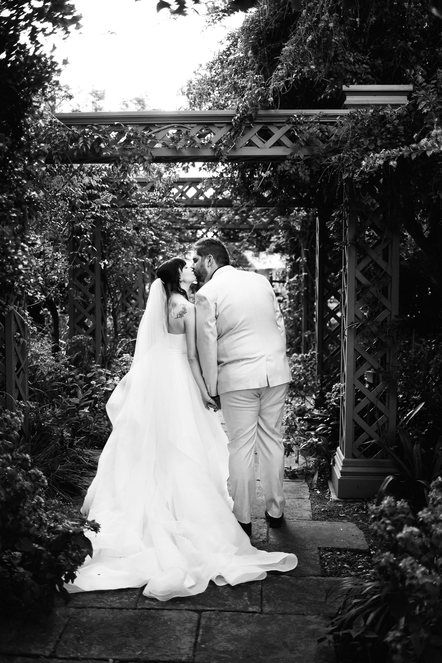 Black and white photo of bride and groom sharing a romantic moment under a garden pergola.