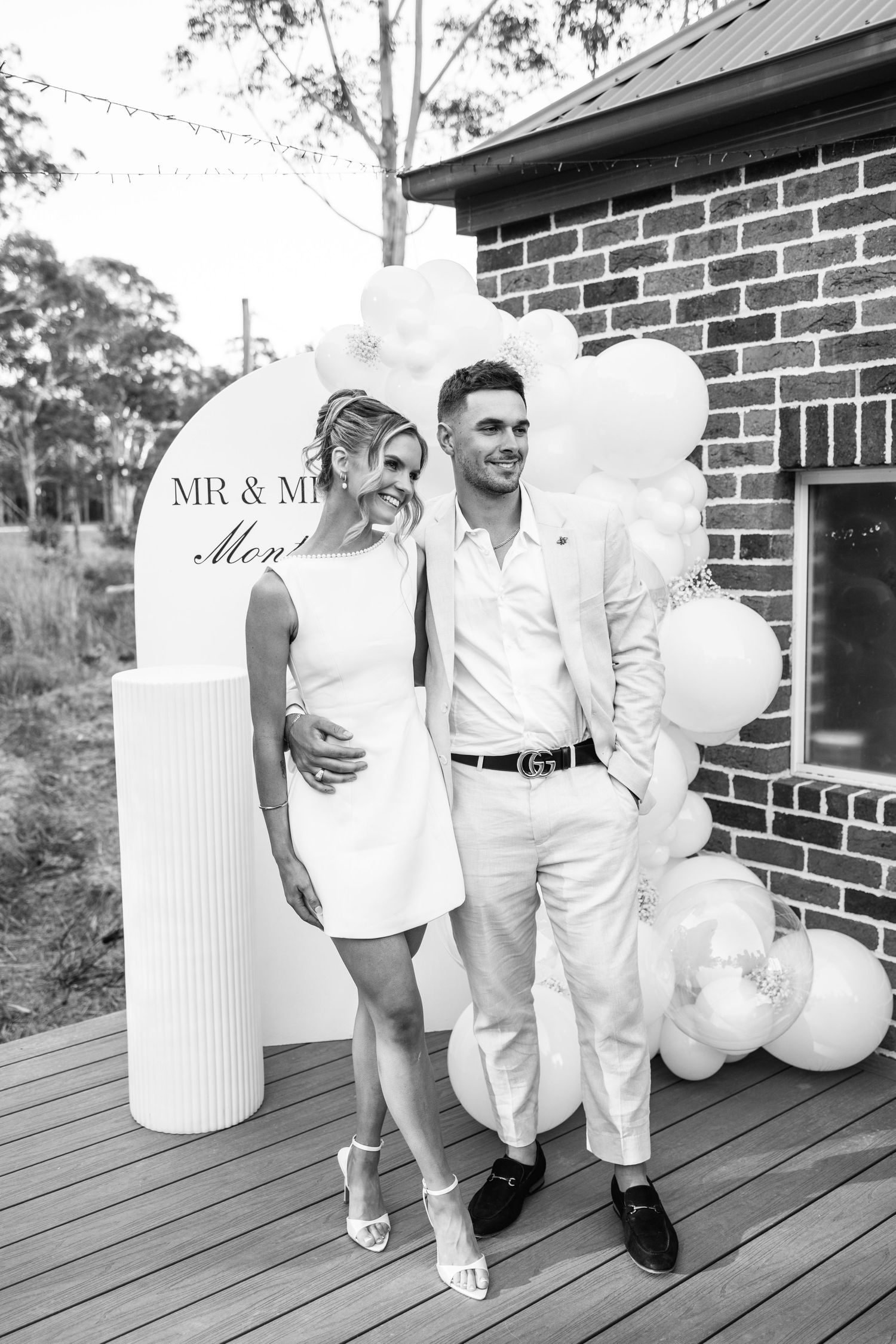 Black and white photo of an engaged couple posing in front of a balloon arch and Mr and Mrs sign.