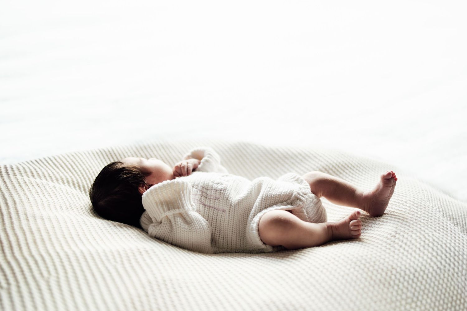 Newborn baby sleeping peacefully on a white textured blanket in a bright, minimalist setting.