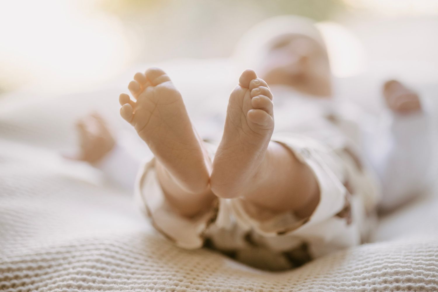 Close-up of newborn baby tiny feet lying on white knit blanket in soft natural light.