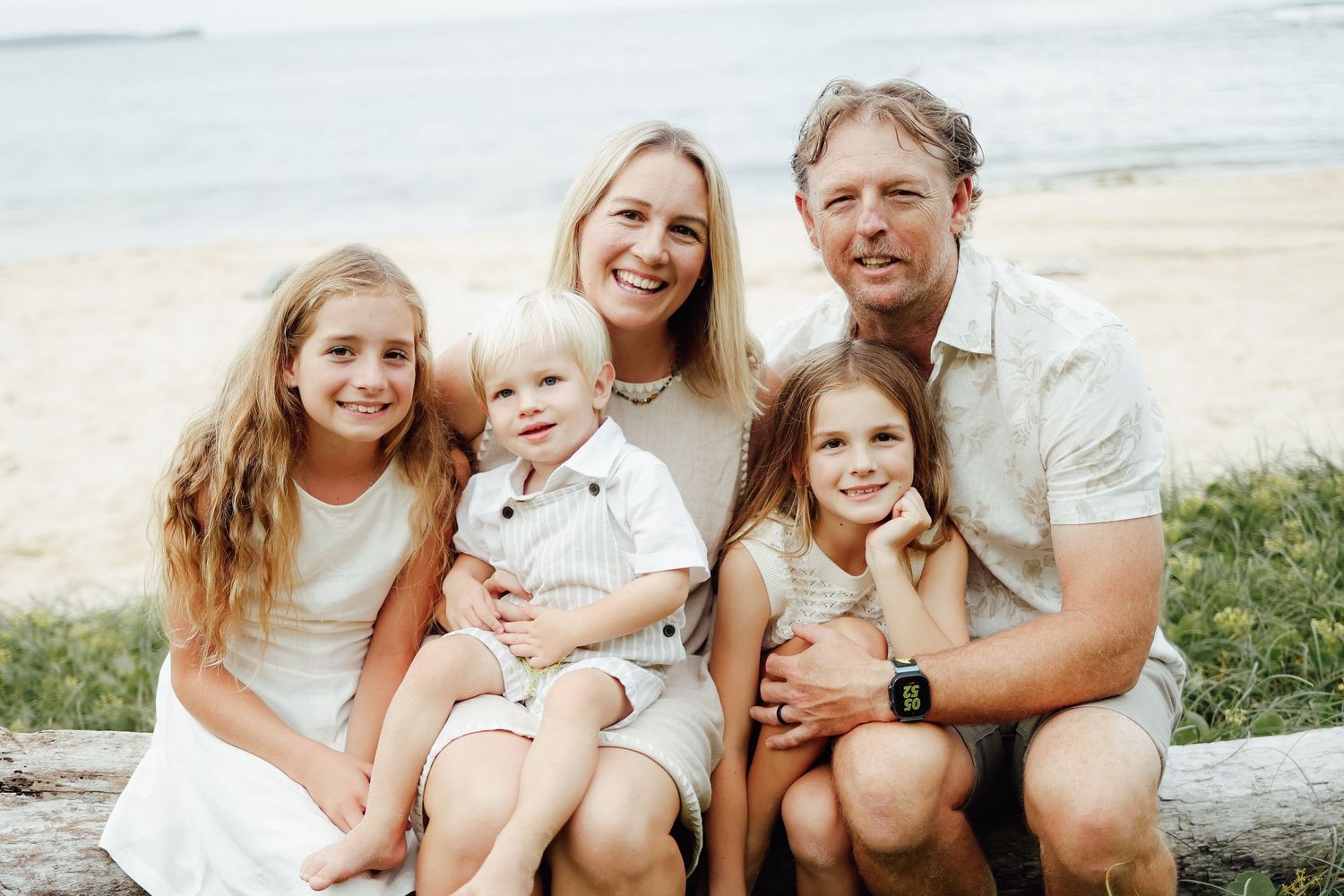 Happy family of five with three children posing together on a sandy beach near the water.