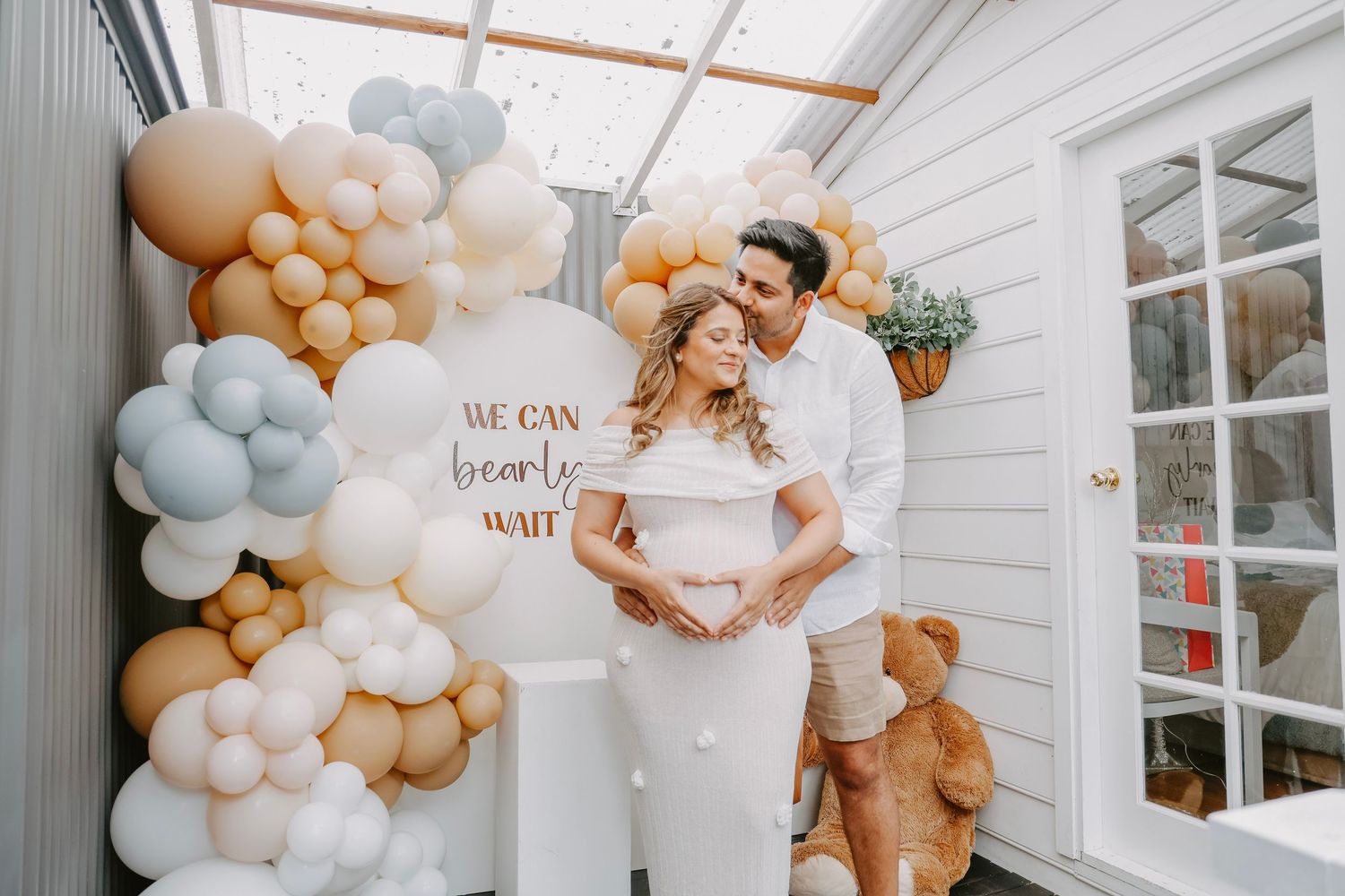 Couple embracing at baby shower decorated with neutral balloons and We Can Bearly Wait sign.