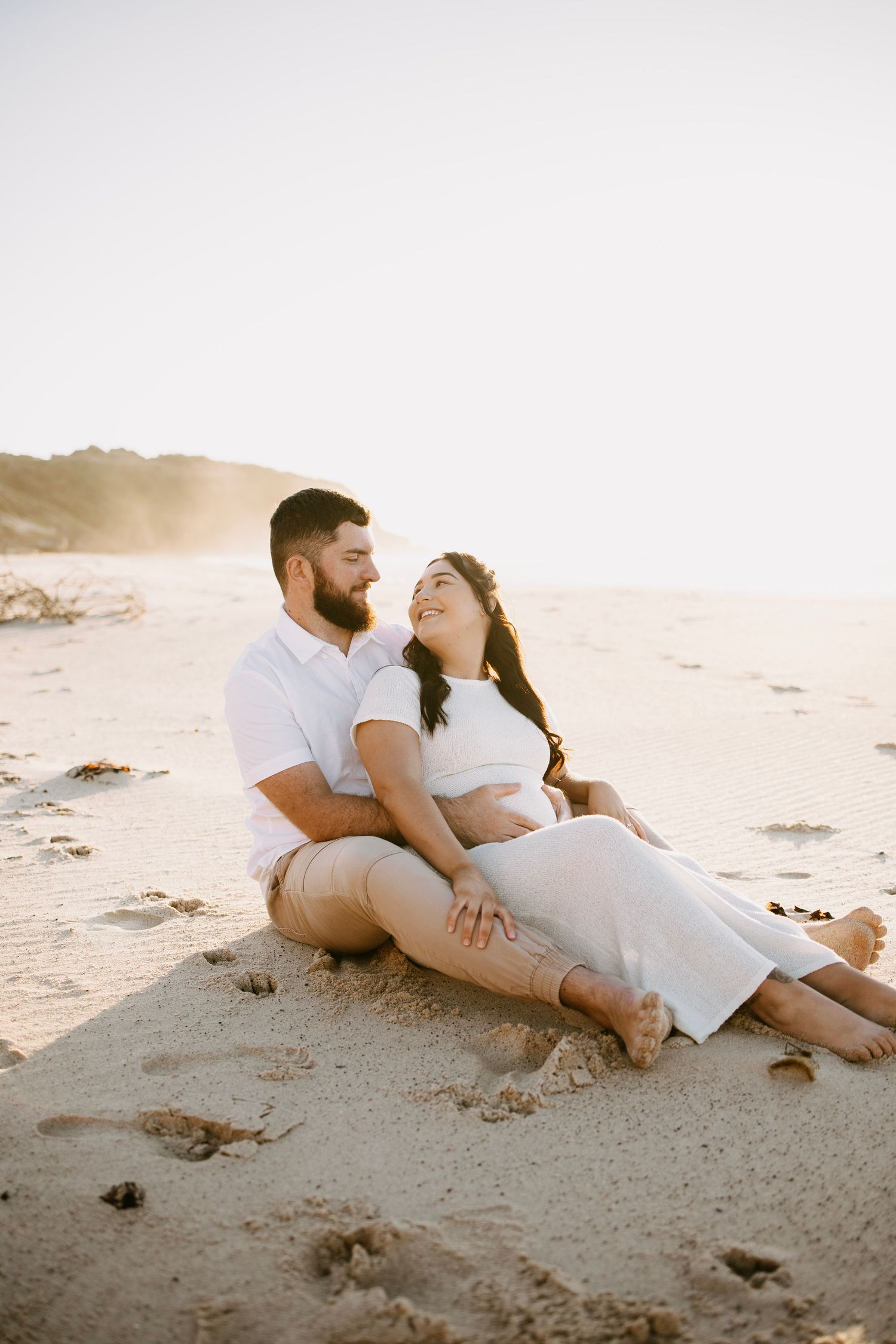 Happy couple sitting together on a sandy beach at golden hour sunset.